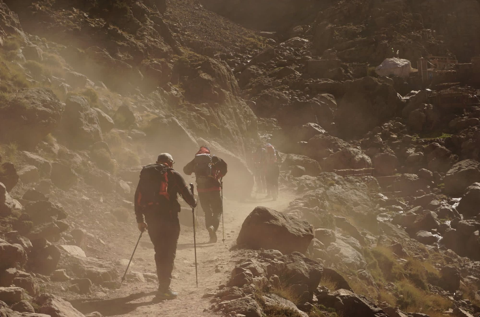 Hikers walking a dusty mountain path below Jebel Toubkal