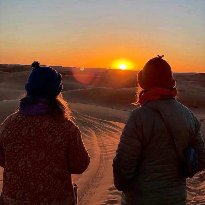 Two guests watching the sun rise over the Sahara dunes