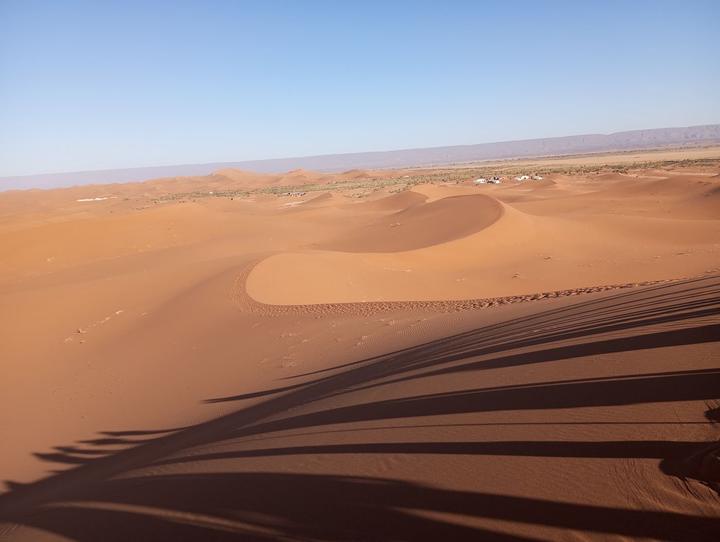 Sand dunes stretching to the horizon with long shadows and a distant camp