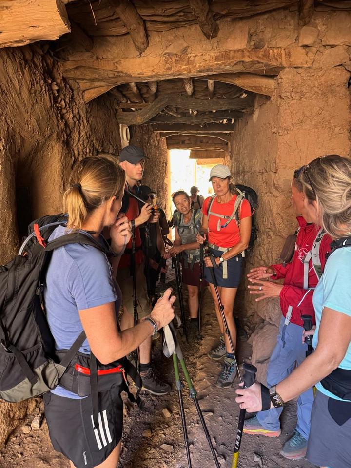 Trekkers listening to their guide inside a covered mud-walled passage in a village