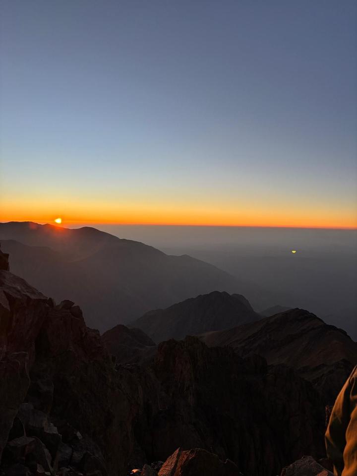 Sunrise over layered mountain ridges seen from a high rocky summit