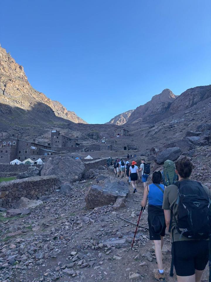 Trekkers walking up a rocky path towards a mountain refuge and tents