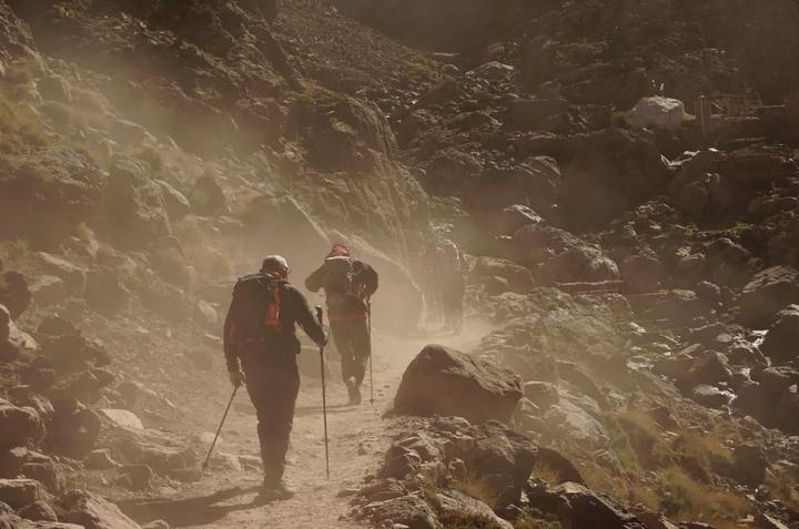 Hikers with poles walking a dusty path below Jebel Toubkal